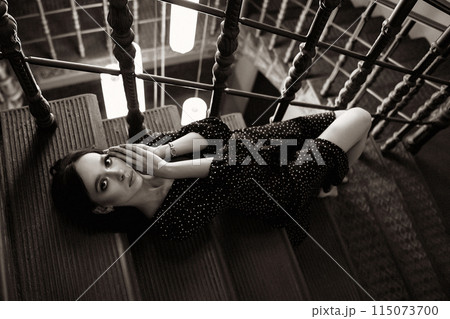 A woman in a black dress is laying on a staircase A woman in a black dress is laying on a staircase 115073700
