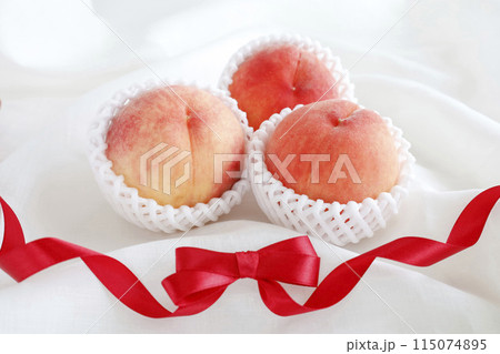 ふんわりソフトな白背景の桃と赤いリボン　贈り物のイメージ 115074895