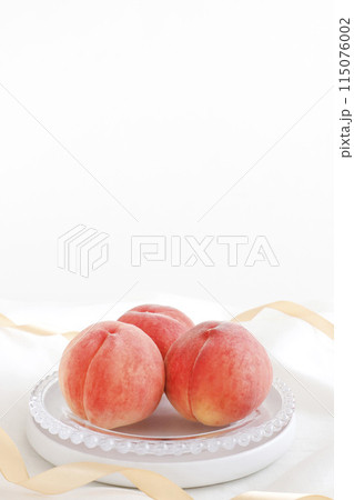 皿に盛られた美味しそうな桃　ゴールドリボンとドレープ布の白背景 115076002