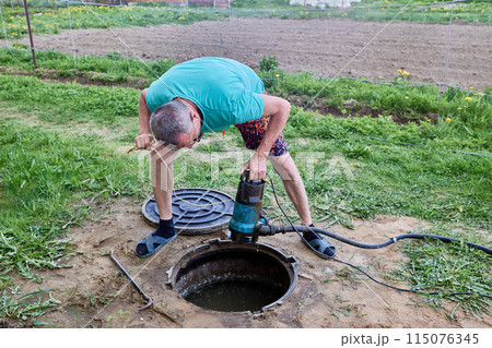 Septic tank is an underground storage tank for sewage waste, worker pumping wastewater with sewer pump. Septic tank is an underground storage tank for sewage waste, worker pumping wastewater with sewer pump. 115076345