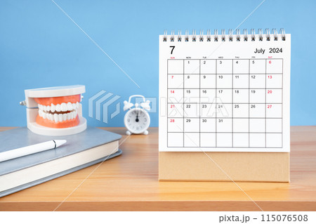July monthly desk calendar for 2024 year and model dentures on the table. 115076508