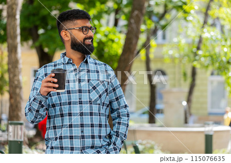 Happy Indian man enjoying drinking morning coffee hot drink, relaxing, taking a break on city street Happy Indian man enjoying drinking morning coffee hot drink, relaxing, taking a break on city street 115076635