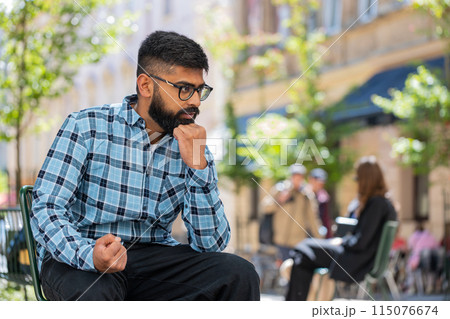 Sad unhappy frustrated Indian man sitting alone in city street, feeling bad, annoyed, grief, problem 115076674