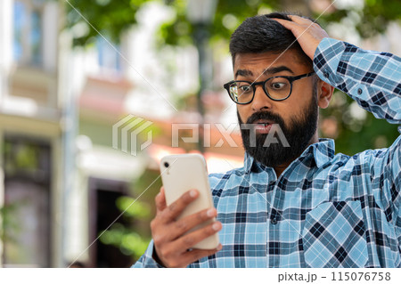 Surprised Indian man use smartphone loses, bad news, fortune loss, fail outdoors in city street Surprised Indian man use smartphone loses, bad news, fortune loss, fail outdoors in city street 115076758