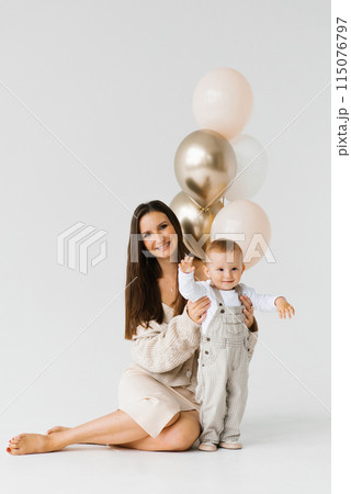 Happy woman and child pose for a photo with golden and white balloons. The scene is happy and joyful Happy woman and child pose for a photo with golden and white balloons. The scene is happy and joyful 115076797