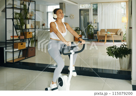 Woman Exercising on Bike in Modern Living Room Woman Exercising on Bike in Modern Living Room 115079200