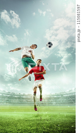 Dynamic image of two soccer players in mid-air, competing to head soccer ball on lush green soccer field, with large stadium filled of fans on background. Dynamic image of two soccer players in mid-air, competing to head soccer ball on lush green soccer field, with large stadium filled of fans on background. 115081597