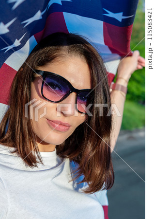 Young woman holding USA flag outdoors at sunset. Independence day. 115083421