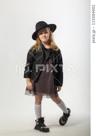 A little blonde girl in a leather jacket and a black hat 115084002