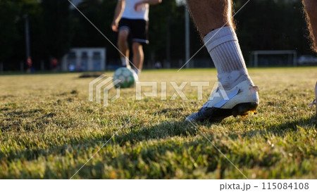 Male feet of professional footballers passing soccer ball on stadium at sunset. Legs of sportsmen kicking ball at green field. Young men training at meadow. Concept of a freestyle football. Slow 115084108