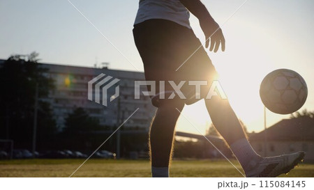 Legs of young man kicking ball at green field. Male feet of professional footballer juggling soccer ball on stadium at sunset. Sportsman practicing tricks outdoor. Concept of a freestyle football Legs of young man kicking ball at green field. Male feet of professional footballer juggling soccer ball on stadium at sunset. Sportsman practicing tricks outdoor. Concept of a freestyle football 115084145