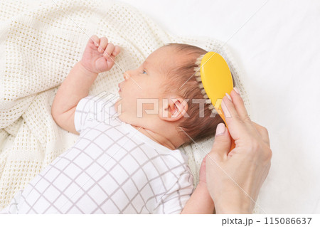 Mother gently brushing her newborn babys hair 115086637