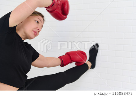 Female boxer stretching arms, warming up her body before boxing training, wearing boxing gloves, isolated over white studio background 115088475