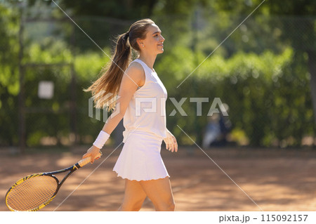 A woman in a white tank top and white skirt is holding a tennis racket 115092157