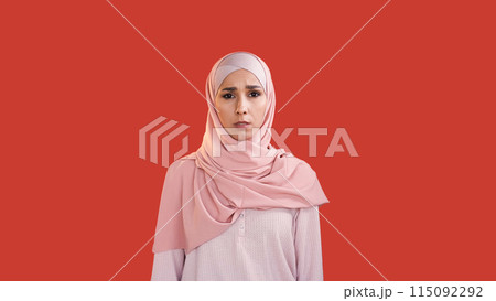 Scared woman. Fear anxiety. Stress problem. Disturbed shocked frightened female face in hijab with open mouth isolated on red copy space background. Scared woman. Fear anxiety. Stress problem. Disturbed shocked frightened female face in hijab with open mouth isolated on red copy space background. 115092292