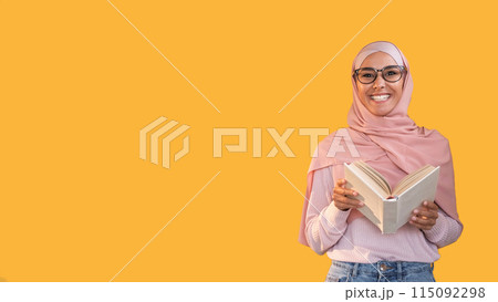 Teacher portrait. Reading class. Study course. Smart cheerful woman in hijab glasses with open book isolated on orange empty space background. 115092298
