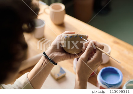 High angle view closeup of unrecognizable woman coloring handmade ceramic vessel 115096511