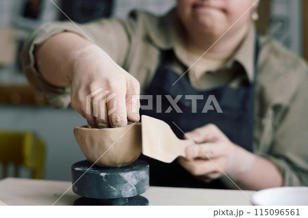 Closeup of hands of unrecognizable woman with Down syndrome making ceramic bowl in pottery class 115096561