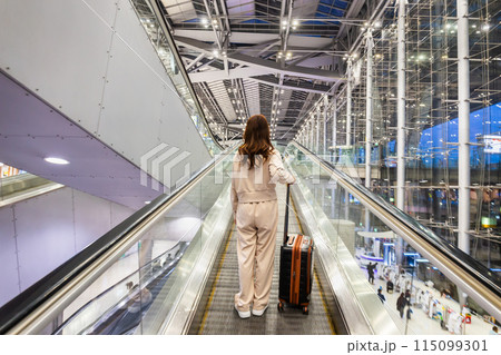 Women drag suitcases up escalators at the airport in preparation to board flights for sightseeing and business trips. Women drag suitcases up escalators at the airport in preparation to board flights for sightseeing and business trips. 115099301