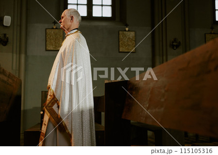Side view medium long shot of senior Caucasian priest wearing liturgical clothes walking along Catholic church nave 115105316
