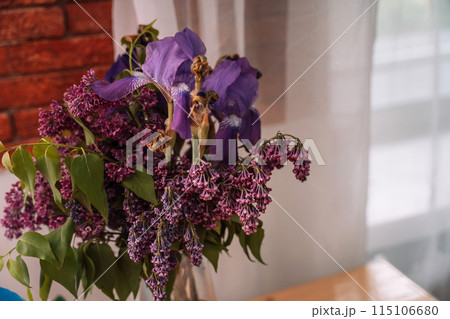 Withered bouquet of lilac and iris flowers in a glass vase Withered bouquet of lilac and iris flowers in a glass vase 115106680