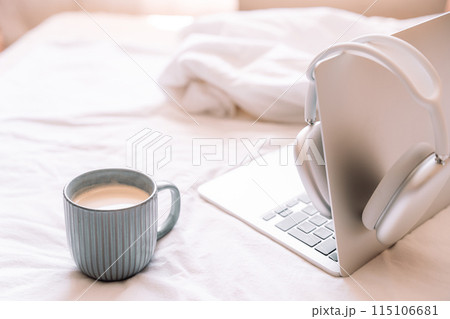 Cozy workplace with wireless headphones hanging on laptop with cup of coffee Cozy workplace with wireless headphones hanging on laptop with cup of coffee 115106681