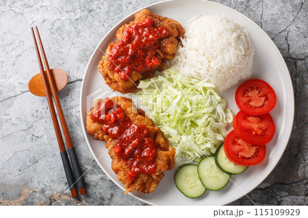 Ayam geprek is a typical Indonesian dish of fried chicken with sambal served with white rice, cucumber, tomato and cabbage closeup on the plate. Horizontal top view Ayam geprek is a typical Indonesian dish of fried chicken with sambal served with white rice, cucumber, tomato and cabbage closeup on the plate. Horizontal top view 115109929