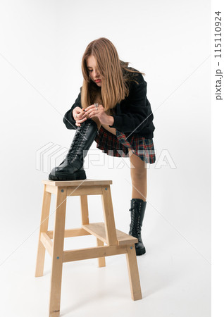 Teenage girl tying shoelaces on white background. Teenager girl in a skirt posing in the studio on a white background. 115110924