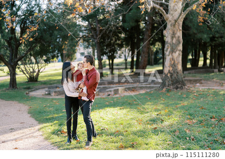 Mom hugs dad with a little girl in his arms kissing her on the cheek Mom hugs dad with a little girl in his arms kissing her on the cheek 115111280