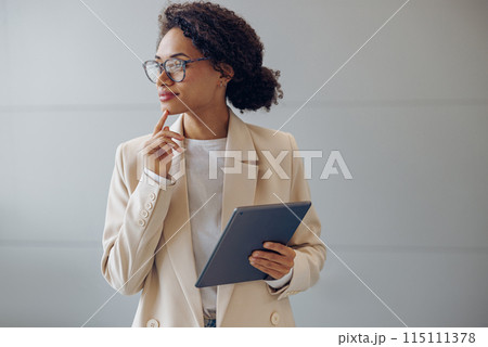 Focused female freelancer with digital tablet standing on coworking background and looks away Focused female freelancer with digital tablet standing on coworking background and looks away 115111378