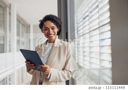 Smiling female manager with digital tablet standing on modern office background and looks camera Smiling female manager with digital tablet standing on modern office background and looks camera 115111449