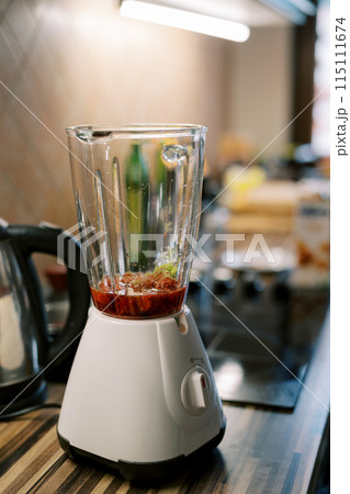 Blender whips up a red drink on a table in the kitchen Blender whips up a red drink on a table in the kitchen 115111674