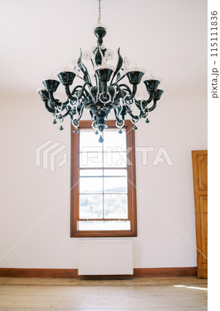 Large black chandelier hangs on the ceiling in the hall opposite the window Large black chandelier hangs on the ceiling in the hall opposite the window 115111836
