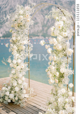 Wedding arch decorated with white flowers stands on the pier. Side view 115111858