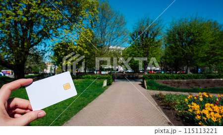 A person is holding a white credit card in a park 115113221