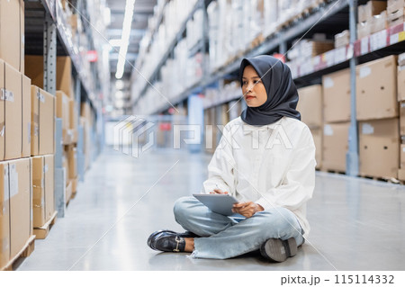 Muslim female wearing hijab warehouse worker holding tablet checks stock on shelf storehouse. 115114332