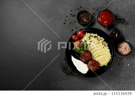 Fried cutlets with mashed potatoes, tomatoes and herbs. Black plate on a black background Fried cutlets with mashed potatoes, tomatoes and herbs. Black plate on a black background 115116439