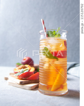 cool peach tea with mint and ice in a glass on a blue background. Front view and copy space cool peach tea with mint and ice in a glass on a blue background. Front view and copy space 115120702