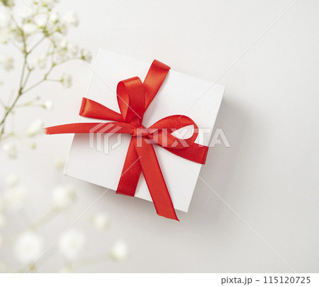 a white gift box with a red ribbon on a white  background with a bouquet of  gypsophila.  115120725
