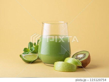 Smoothie made of green kiwi fruits, apple, lime and mint in a glass on a yellow background.  115120754