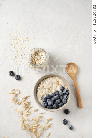 Oatmeal porridge with blueberries in bowl  with wooden spoon and  jar of oats flakes   115120782
