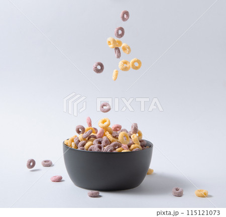 sweet colorful cornflakes rings fly in a black bowl on gray background. Front view and copy space sweet colorful cornflakes rings fly in a black bowl on gray background. Front view and copy space 115121073