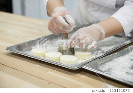 A woman makes cheesecakes by hand in production. Factory for the production of food. 115121076