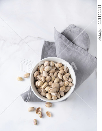 Pistachio nuts in a white bowl on a napkin and  marble background. Top view and copy space 115121111