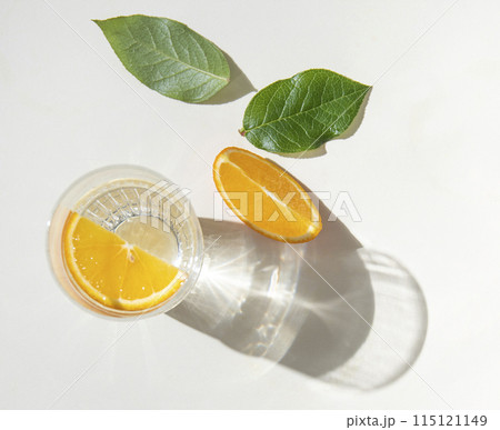 A glass of mineral water and a slice of orange on a light table with fresh juicy fruit oranges A glass of mineral water and a slice of orange on a light table with fresh juicy fruit oranges 115121149