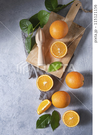 A few juicy oranges cut on a wooden board with green leaves on a blue background. A few juicy oranges cut on a wooden board with green leaves on a blue background. 115121156