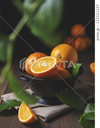 A few juicy oranges in a black bowl with green leaves on a dark wooden background A few juicy oranges in a black bowl with green leaves on a dark wooden background 115121157