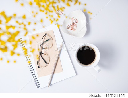 Flat lay with yellow mimosa flower, cup of coffee, a glasses, a craft notebook on a marble table. Flat lay with yellow mimosa flower, cup of coffee, a glasses, a craft notebook on a marble table. 115121165
