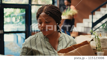 Buyer enjoying fresh smell of locally grown lemons from farm, smelling citric aroma and putting ecological fruits in a bag. African american client looking for homegrown goods. Tripod shot. 115123006