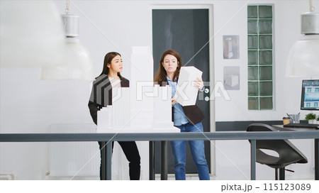 Experts measure models printed in 3D to determine proportions while working on unicorn business expansion goals. Women builders develop architectural blueprints using scale dimensions. 115123089